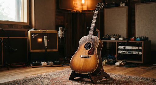 A vintage acoustic guitar resting on a stand in a warmly lit studio space